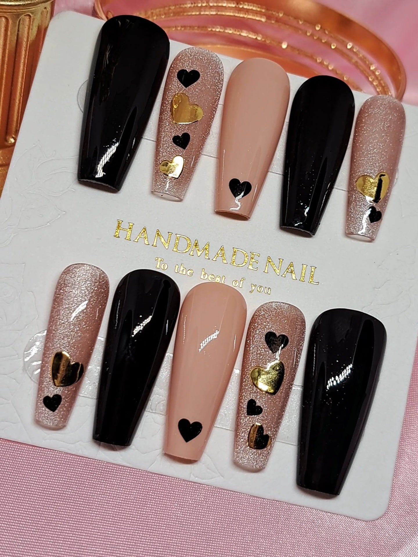 A set of press on nails featuring a variety of designs, including hearts and the color sequence from black to nude.